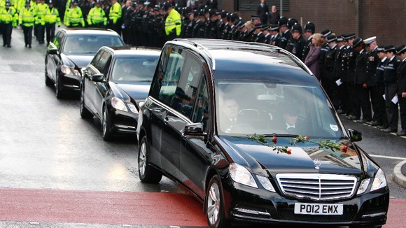 Roses rest on the bonnet of the hearse carrying the coffin