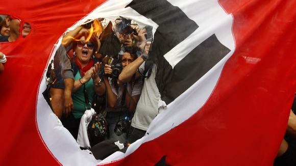 Demonstrators burn a flag emblazoned with a swastika during a demonstration against the visit of German Chancellor Angela Merkel