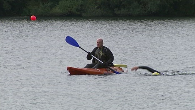 A soldier swimming next to a canoe.