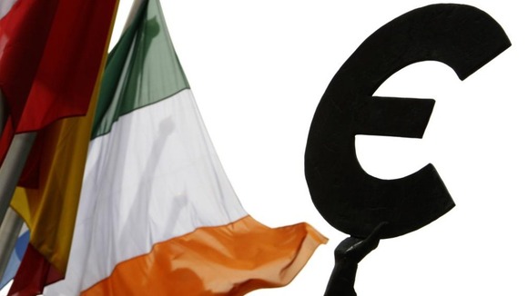 An Irish flag flies next to a symbol of the euro currency at the entrance of the European Parliament in Brussels,