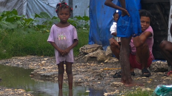 A Haitian girl stands in dirty water after heavy rains from Hurricane Sandy flooded her tent encampment