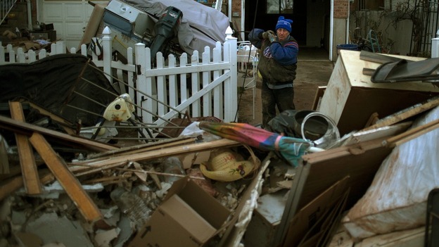 A man carries his belongings to a pile outside his house, which was left flooded by hurricane Sandy, in Staten Island