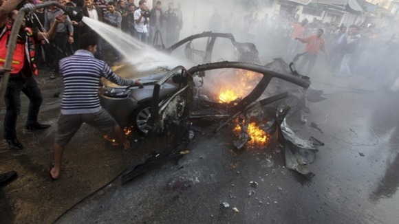 Palestinians help extinguish the fire on the car of Hamas's top commander after an Israeli airstrike
