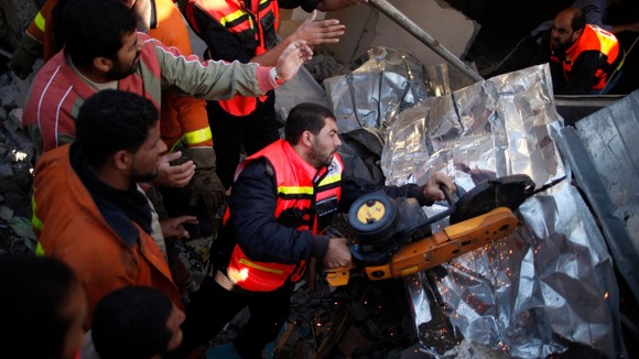 Palestinian Civil Defense members cut through metal as they search for victims under rubble