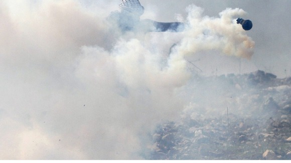 A Palestinian stone thrower throws a tea gas grenade back to Israeli troops