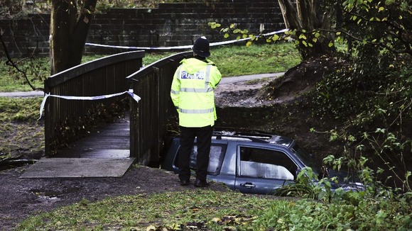 Police officer examines the scene where a man died after his car became trapped in flood water