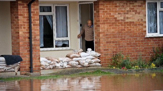 An elderly man keeps an eye on sandbags and the water level outside his property.