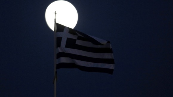 A Greek flag flutters in front of the moon in Athens
