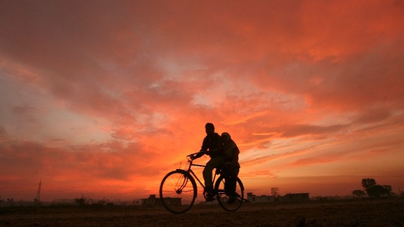 Two people ride a bicycle as the sun sets on the outskirts of Jammu in India.