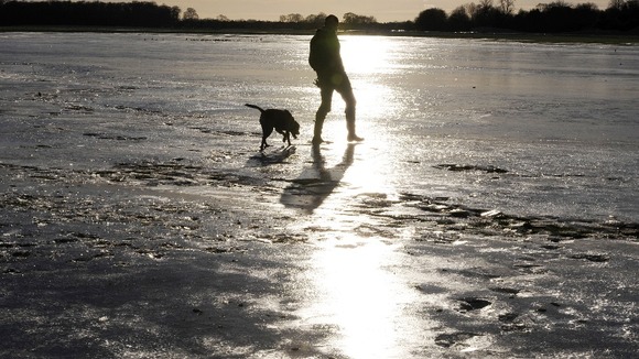 A man walks his dog on frozen flood water at York Knavesmire, North Yorkshire