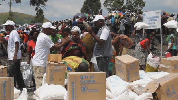 Food aid bags and boxes of oil are given out to those queuing at UN camp