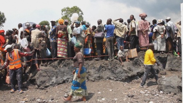 People displaced by recent fighting line up on lava rocks