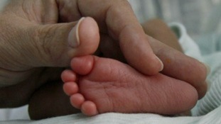 A doctor touches the feet of a premature baby lying in an incubator.