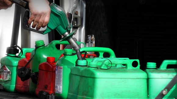 A man uses petrol pumps to fill petrol cans