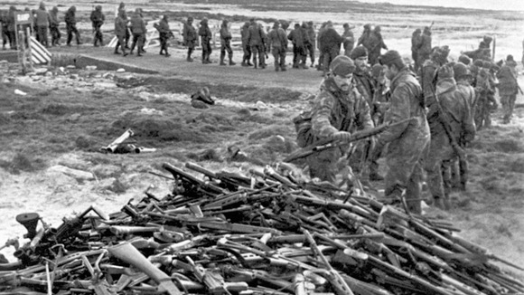Argentine soldiers line up to hand in their weapons to Royal Marines near Port Stanley.