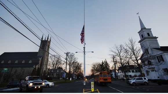 A US flag flies at half mast as a school bus drives past in the town of Newtown on the day of the shootings a week ago