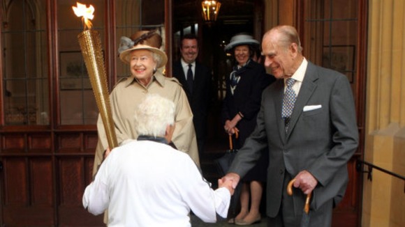 The Queen looks at the Olympic Flame as the Duke of Edinburgh shakes hands with torchbearer Gina Macgregor at Windsor Castle