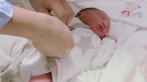 hands seen doing up buttons on clothes of new born baby