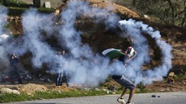A masked Palestinian protester uses a sling to throw back a tear gas canister