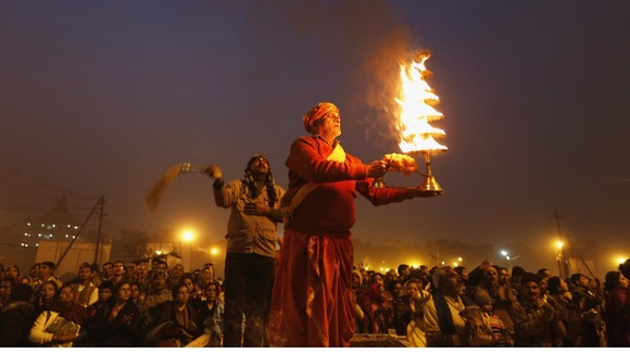 A Hindu priest holds oil lamp as performs evening prayers near the banks of the River Ganges