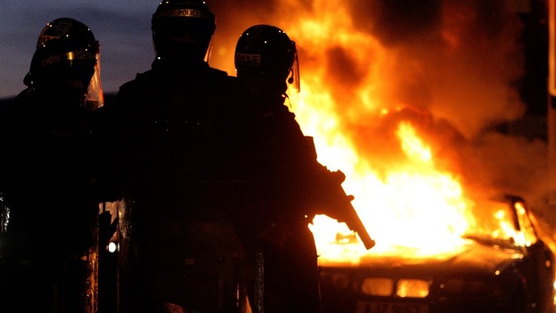 Riot police stand next to a burned out car in east Belfast