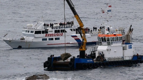 Workers drop a stone with a plaque into the sea during a ceremony to commemorate the first anniversary of the Costa Concordia tragedy