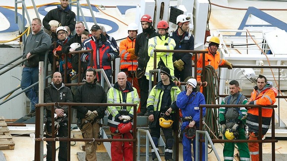 Salvage crew workers stand on a side of the capsized cruise liner Costa Concordia as they pay respects to the deceased