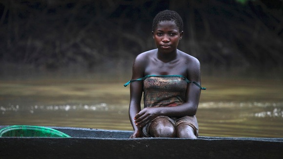 A young woman is pictured coated in oil stains as she sits in a canoe near river Nun in Nigeria's oil state of Bayelsa
