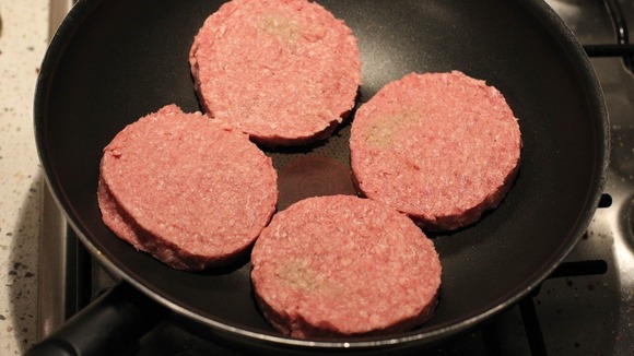 A general view of four beef burgers in a frying pan.