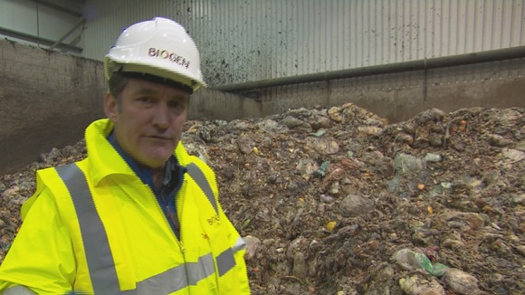 man in safety jecket and helmet in front of mound of food waste