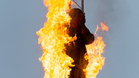 One of the team is on fire at the top of a high tower, before jumping.