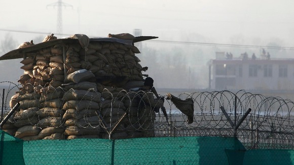 An Afghan police officer keeps watch as members of the Afghan security forces run on the roof