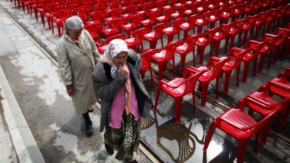 Women walk past some of the red chairs ahead of the official start of events for the 20th anniversary