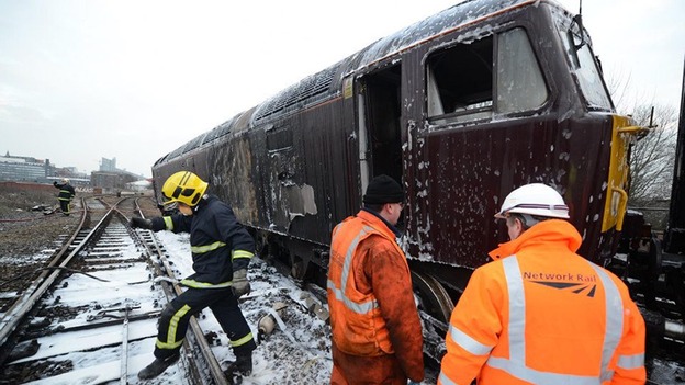 Workers and firefighters on the track after a train comes off the rails and catches fire in Manchester city centre