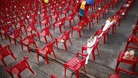 A child places a flower on a small chair symbolizing children killed