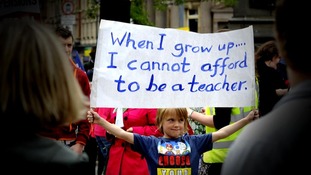 A boy holds up a banner saying: When i grow up I cannot afford to be a teacher'