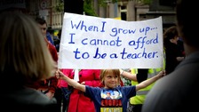 A boy holds up a banner saying: When i grow up I cannot afford to be a teacher'