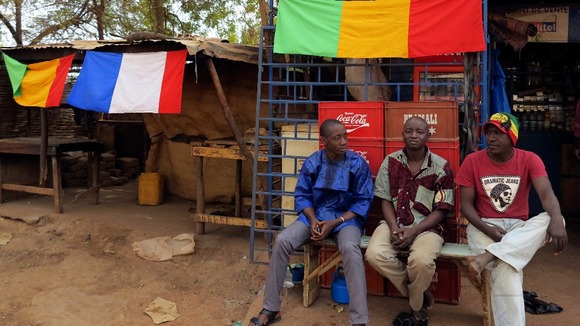 Men sit outside a shop as Malian and French flags decorate the area in Sevare, near Gao.