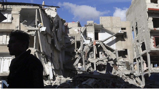 A Free Syrian Army fighter stands in front of a building destroyed by a Syrian Air force air strike in Damascus