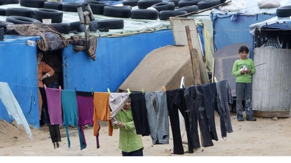 A Syrian child looks through clothing hanging on a line at a refugee camp 