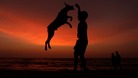 A boy plays with his pet on a beach as the sun sets in Colombo