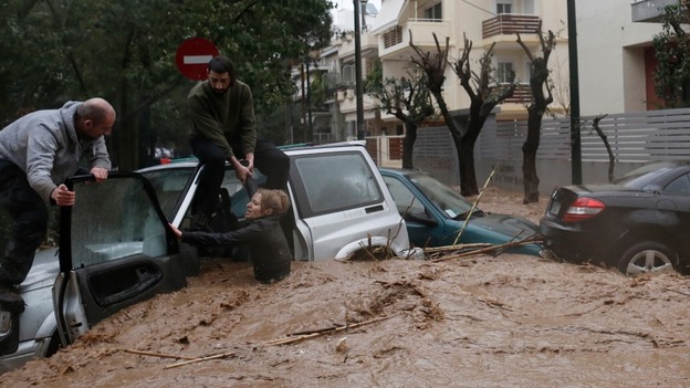 A woman stuck in her car is rescued from flood waters by residents in the Greek capital.