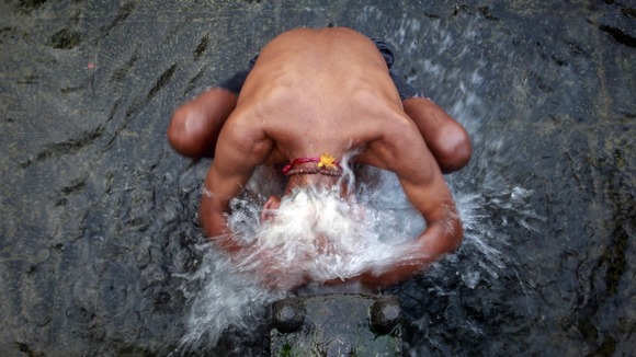 Water splashes over the head of a devoted man as he washes in the holy water