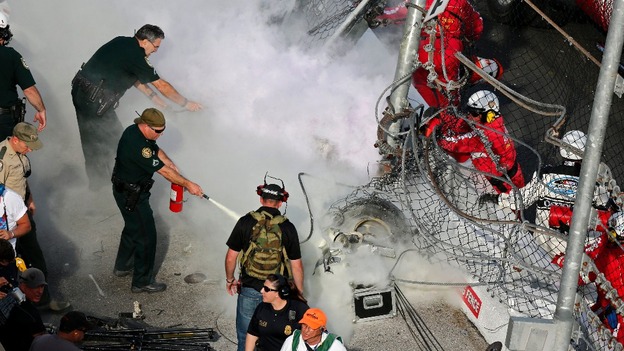 Fire crews put out a blaze as one of the engines in the accident burns through the catch fence
