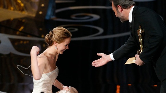 Jennifer Lawrence is helped by presenter French actor Jean Dujardin after she tripped