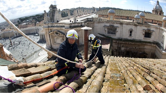 Under sunny skies fire-fighters set up the chimney on the roof of the Sistine chapel ahead of the cardinals conclave