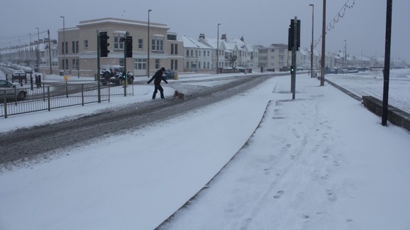 Person and dog crosses snowy road in Worthing