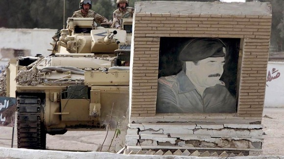 A British Warrior armoured combat vehicle drives into a picture of Saddam Hussein in the city of Basra.