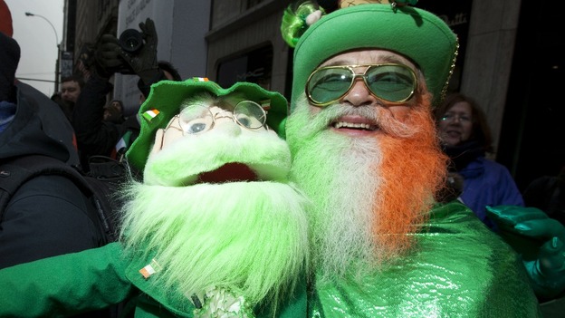 A man wears fancy dress and carries a puppet as he watches the parade.