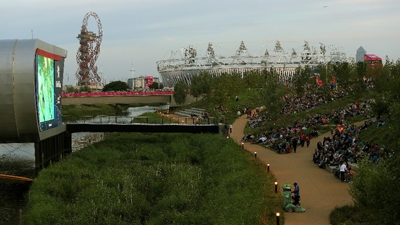 People sit in the Olympic Park and watch the swimming event on a huge TV-Screen in front of the Olympic Stadium during the Games